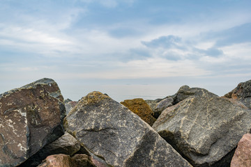 Granite revetment or seawall on the shore. Huge stones to protect beach from erosion. Prevent disaster. Copy space. Blue cloudy sky.