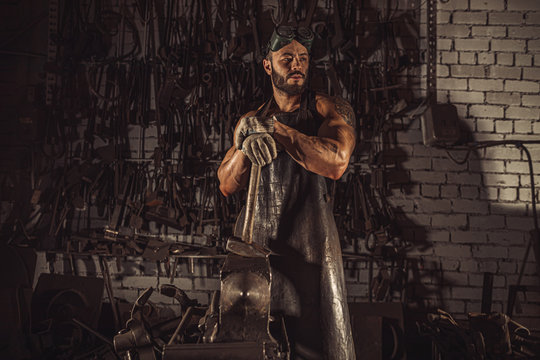 young blacksmit work with hammer isolated in workshop, young forger in leather apron