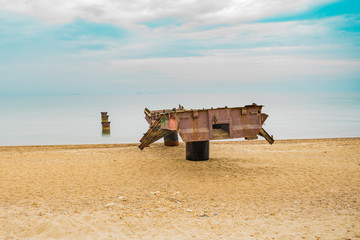 Fototapeta premium Abstract sea monster getting out of the water. Boat launching rail ramp destroyed by erosion. Seascape. Funny bridge with eyes, mouth and paddles or wings. Vivid azure sky.