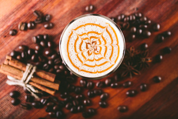 The glass cup of latte coffee with coffee grains and cinnamon sticks decoration stands on wooden table. Top view.