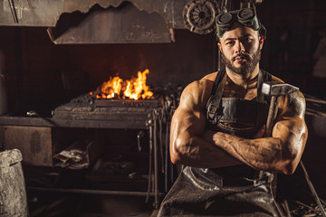 Portrait of serious confident strong young metalworker in black apron stand looking at camera, work in workshop