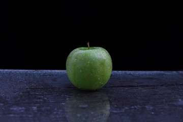 Green, ripe, juicy Apple on dark background and glass kitchen table with water drops and empty space for text
