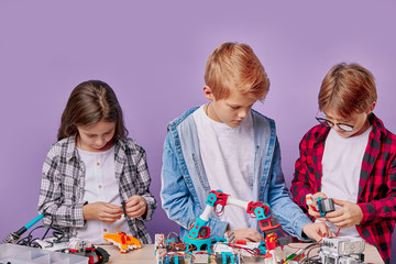 portrait of enthusiastic three kids working as team, assembling robots. three future engineers look...