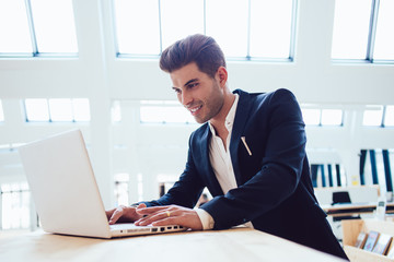 Cheerful caucasian businessman in formal wear satisfied with trading on web pages earning money online, smiling prosperous male entrepreneur  using laptop computer for reading news about exchange