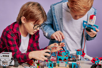 close-up portrait of boys diligently assembling robots, careful kids connectng wires of robot toys....