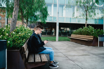 Fototapeta premium Young man sitting on bench with smartphone