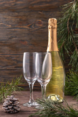 Beautiful holiday card. Bottle of champagne prepared for the holiday with two glasses on a wooden background. Decorations for the new year of fir and cones.