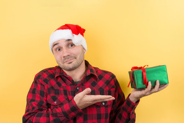 Happy surprised man in a red hat holding a gift with admiration on his face. Positive human emotions at christmas. Yellow background, copy space.