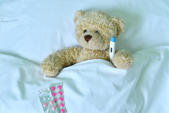 Teddy bear with a electronic thermometer in bed
