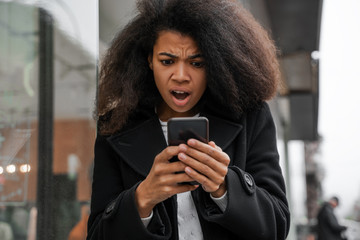 Oh my god, a girl looks in surprise at the phone with a shocked expression on her face, a reaction to a message or news about a cash flow to a bank account