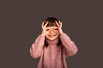 A small playful child plays a game and shows a gesture that she is a pilot of an airplane, on a gray background. Happy carefree and free baby girl