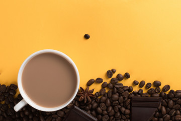 Coffee beans are scattered on a yellow paper background and a white cup, chocolate, concept, commercial copy space.