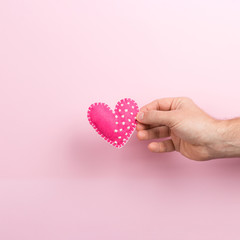Male hand holding a handmade heart on a pink background. Valentine's day concept, symbol of love, print commercial blank, copy space.