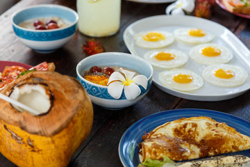wooden brown cracked table set with Breakfast of natural healthy food, scrambled eggs, oatmeal, omelette with vegetables, fruit, coconut in foreground.
