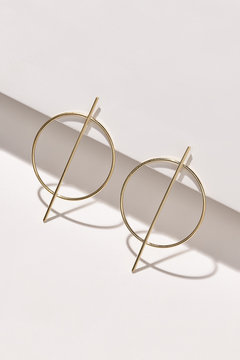 Subject shot of a pair of stud earrings isolated on the white geometric design surface. Each metal earring is made as a golden ring decorated with a golden stick.