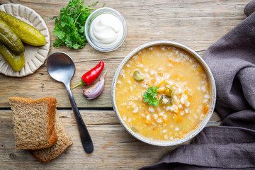 Soup with pickled cucumbers and pearl barley - rassolnik on wooden background, top view