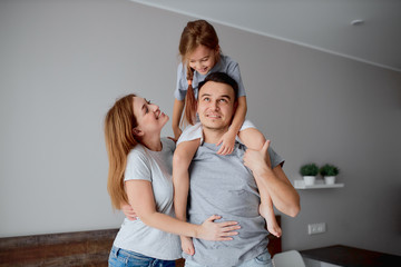 cheerful young caucasian family, parents with daughter, posing at camera isolated in bedroom, hug each other