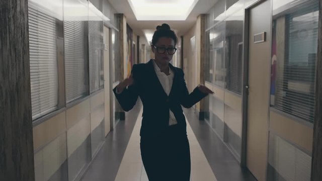Happy joyful young and attractive businesswoman in formal suit dancing victory dance in corridor or hall of modern business center. Female office worker have fun at work place