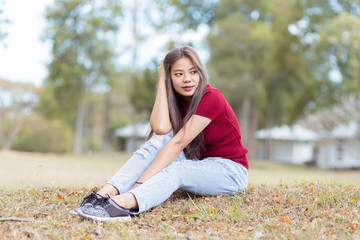 Beautiful Asian women in red dresses and blue jeans sitting in the garden. Portrait of asian woman is smiling on the green grass.