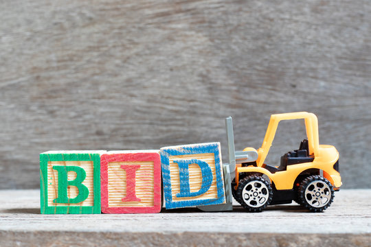 Toy forklift hold letter block d to complete word bid on wood background