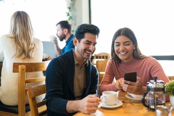 Couple Checking Photos On Smartphone At Cafe