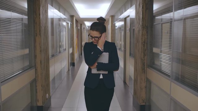 Attractive young caucasian business woman walking in depression with serious face sad along office corridor. Businesswoman holding documents in despair after failed project or meeting. Looking upset