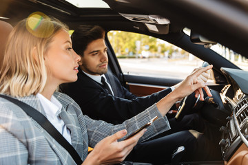 Photo of man and woman talking and using cellphone while driving in car