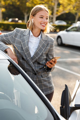 Photo of businesswoman using earpod and cellphone while leaning on car