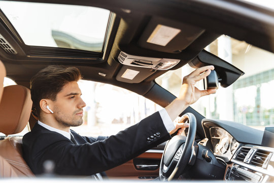 Photo of focused young businessman using earpod while driving car