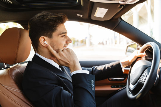Photo of smiling young businessman using earpod while driving car