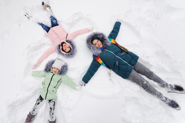 family-mother and two daughters lie on the snow, laughing and making a snow angel. Winter...