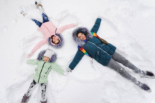 family-mother and two daughters lie on the snow, laughing and making a snow angel. Winter entertainment