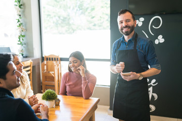 Smiling Waiter With Customers At Cafe