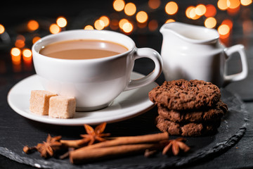Chocolate cookies, coffee, spices on a background of Christmas lights.