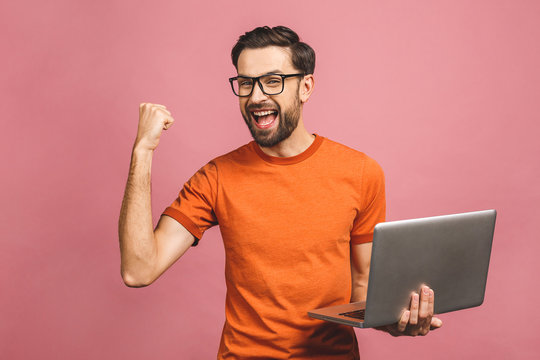 Image of happy excited young man posing isolated over pink background wall using laptop computer make winner gesture.