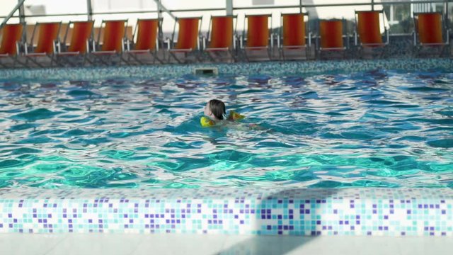 Child in swimming armbands swims in the pool in the hotel, slow motion, outdoor activities