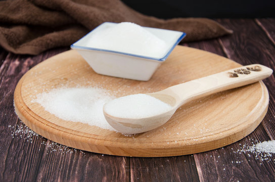 Bowl and spoon with sugar on a wooden background
