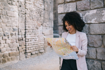 Smiling black woman reading map near stone wall