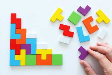 man's hand holding a square tangram puzzle, over wooden table