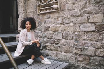 Smiling lady sitting on stairs near aged building