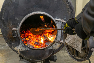 Worker mixes burning ash in a furnace for heating.