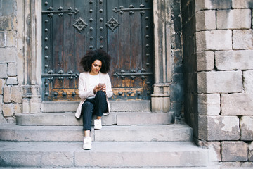 Fototapeta na wymiar Black woman surfing Internet on smartphone and sitting on stone steps