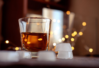 A glass of whiskey or rum with ice on a dark and bokeh background