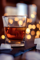 A glass of whiskey or rum with ice on a dark and bokeh background
