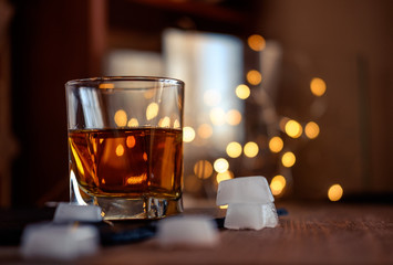 A glass of whiskey or rum with ice on a dark and bokeh background