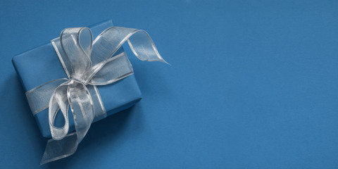 Blue giftbox with silver ribbon on classic blue surface. Space for wishes. Birthday card.