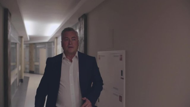 Senior caucasian businessman running along office corridor in deapair. Office worker in formal suit is late for work and hurrying to business meeting