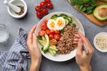 woman eating healthy vegan lunch bowl with avocado, egg, cucumber, tomato and buckwheat