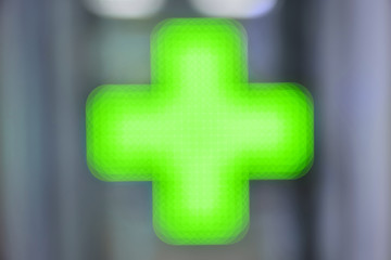 Green medical cross - blurry lights of the pharmacy.