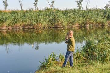 A joyful and happy boy rejoices at his first catch of fish on a fishing rod on the river.